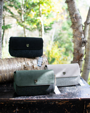Three bags in black, green, and gray on a wooden surface with a forest background