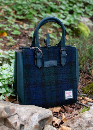 Blue plaid handbag with a visible brand label on a natural background of rocks and plants.